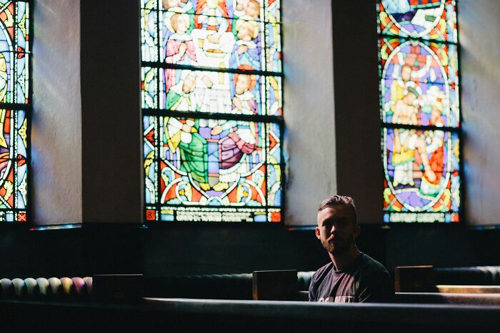 Man sitting in a church pew with colorful stained glass windows in the background, reflecting judgment theme.