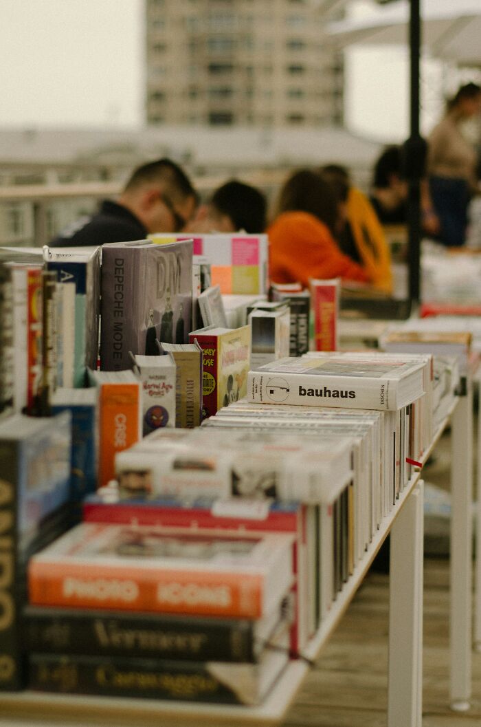 Books displayed on a long table at an outdoor event, with people browsing in the background.