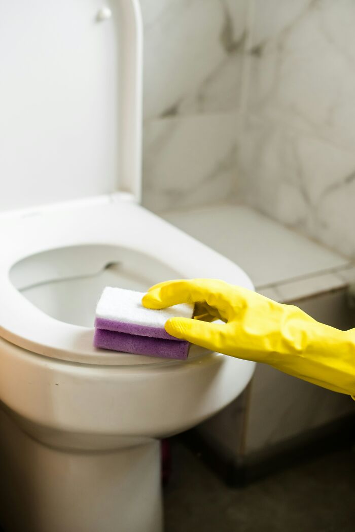 Gloved hand cleaning a toilet with a sponge, illustrating rich kids' unfamiliarity with chores.