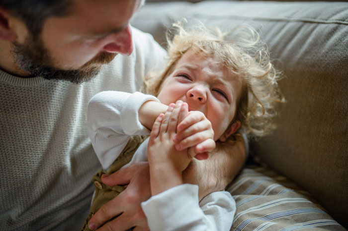 A man comforting a distressed child on a couch, emphasizing family dynamics.