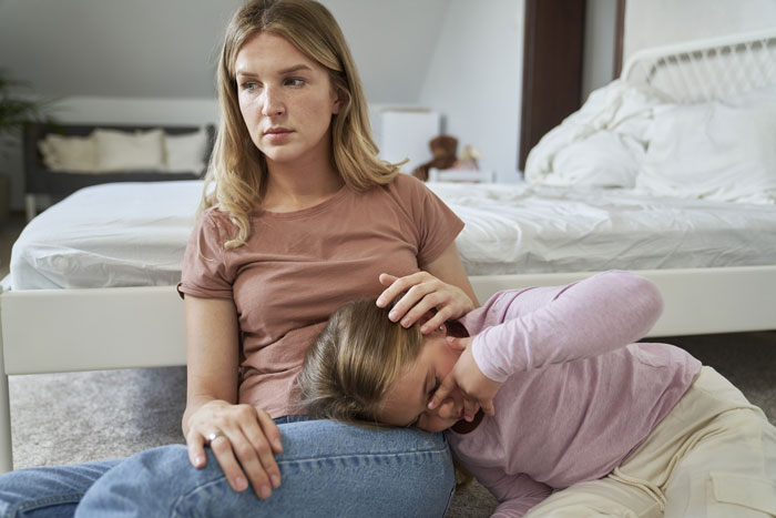 A woman sitting on the floor, comforting a child, both looking bothered.