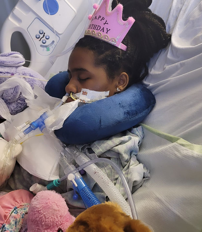 Kelaia Turner recovering in hospital bed with medical equipment, wearing a birthday crown.