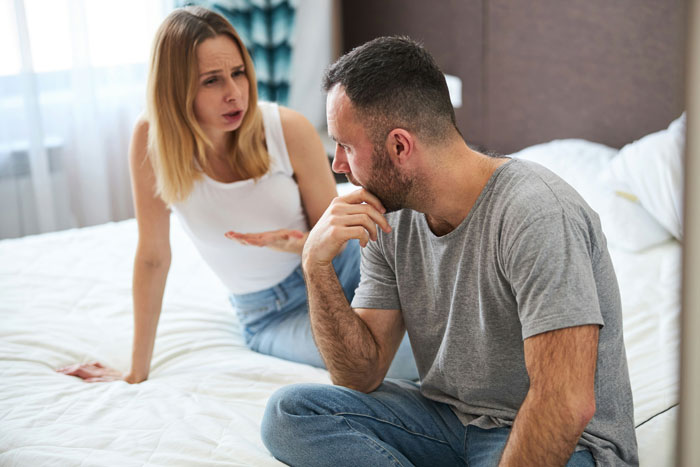 Parents discussing kids' birthday candle tantrums, sitting on a bed in a casual setting.