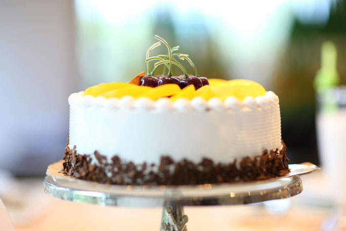 Cake topped with peaches and cherries on a stand, related to kids-revenge-sil theme.