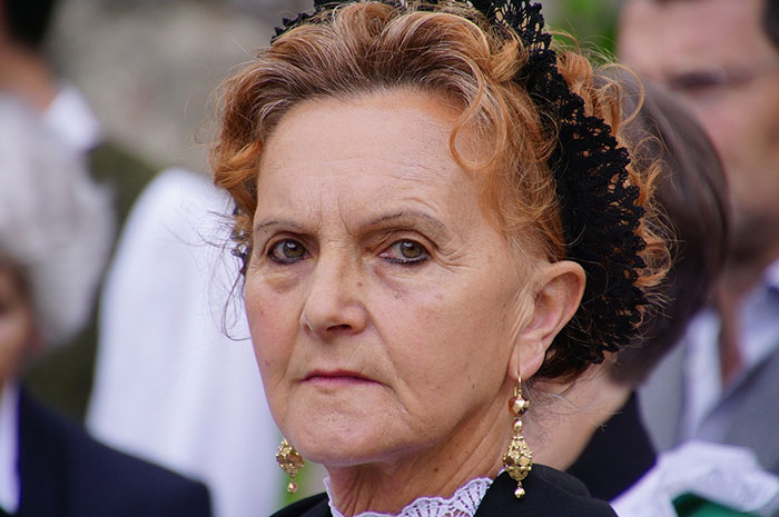 Elderly woman in a black outfit with lace, reflecting on funeral costs and life insurance repayment.