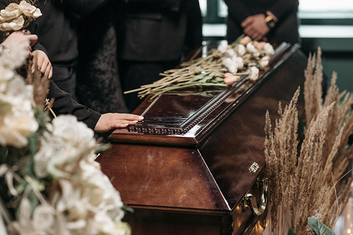 Funeral scene with a hand on a wooden casket and flowers, related to life insurance repayment discussion.