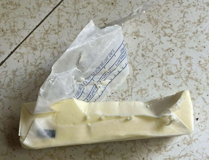 Partially unwrapped stick of butter carelessly left on a kitchen counter, symbolizing lazy-infuriating-people habits.