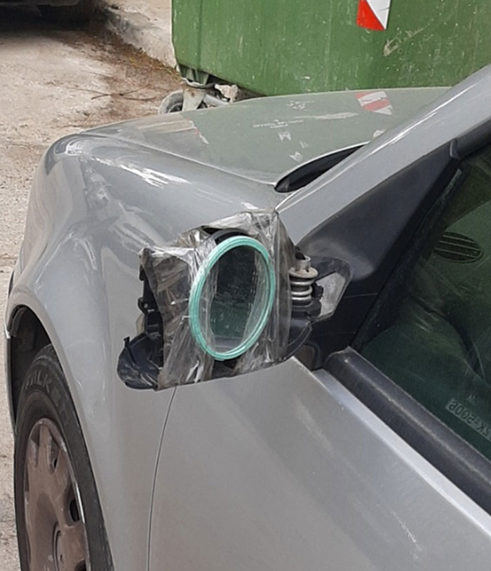 Car with a makeshift side mirror made from a taped plastic plate, showcasing lazy-infuriating creativity.