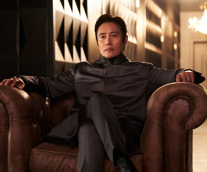 Actor in a black suit sitting on a leather chair, related to "Squid Game 2" cast controversies.