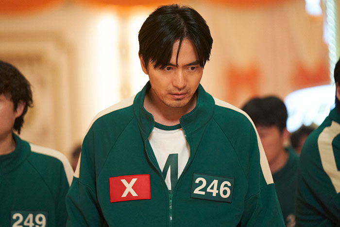 Cast member in green track jacket with number 246 from Squid Game 2, amidst controversy and fan backlash.