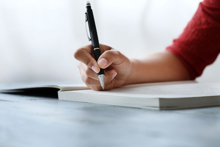 Left-handed person writing in a notebook, showcasing struggles with pen grip on a smooth surface.