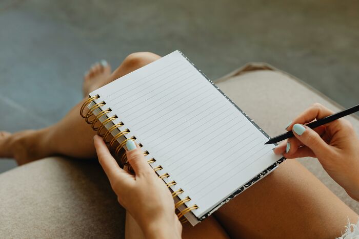 Left-handed person writing in a spiral notebook with a black pen, facing difficulties.