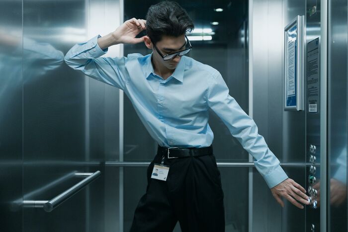 Left-handed person in an elevator, wearing sunglasses, and pressing buttons awkwardly.