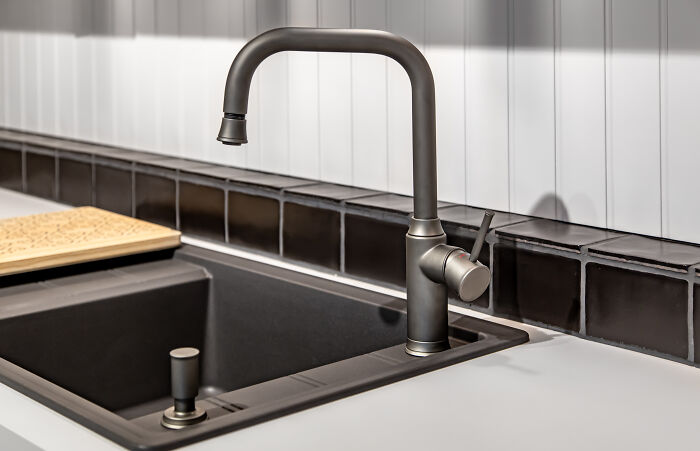 A kitchen sink with faucet and soap dispenser, showcasing left-handed people struggles with right-handed design.