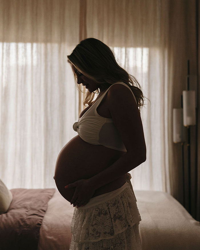 Pregnant woman in silhouette beside bed, showcasing motherhood journey.