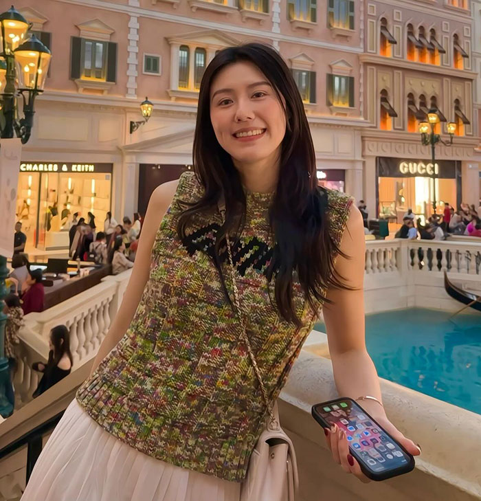 Former Chinese athlete smiling in a stylish outfit, standing by a canal in a shopping mall. Gucci store visible in background.