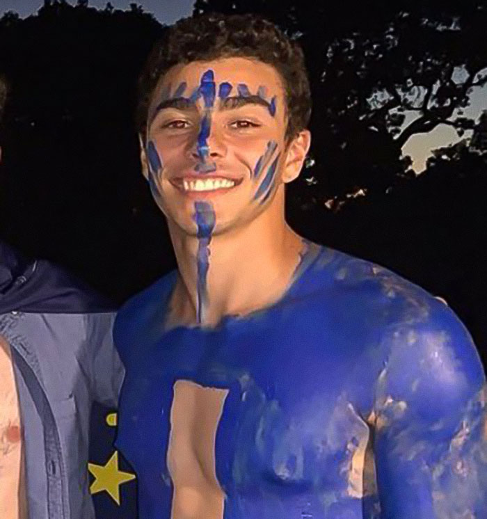 Luigi Mangione with blue body paint and a smile, standing outdoors.