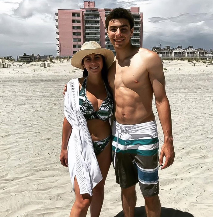 Luigi Mangione and his sister posing on a sandy beach with a pink hotel in the background.