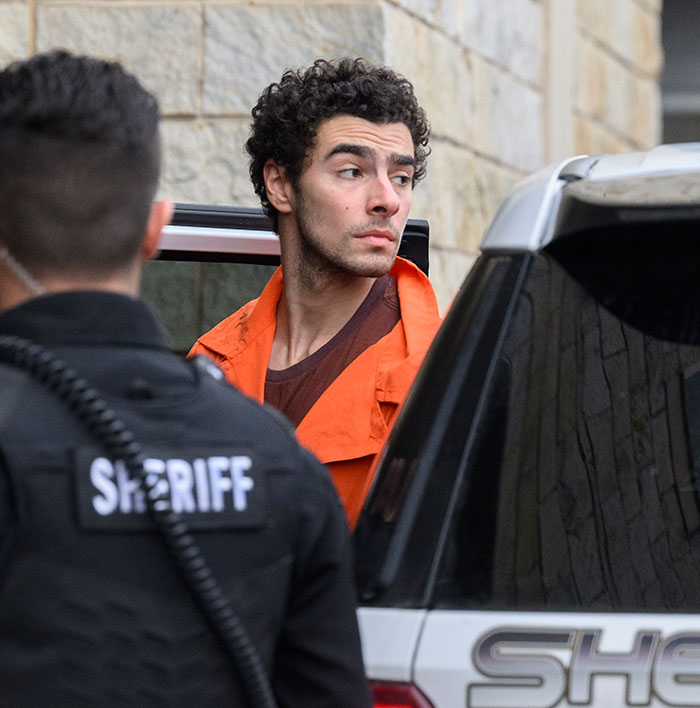 Luigi Mangione in an orange jumpsuit escorted by a sheriff, related to Luigi Mangione's manifesto leak by an American reporter.