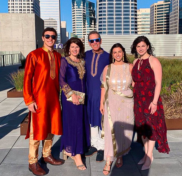 Luigi Mangione family in vibrant attire posing on a rooftop with city buildings in the background during a sunny day.