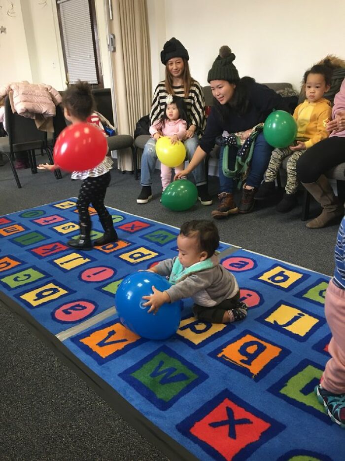 Children playing with balloons on an alphabet mat during a parenting-genius-tricks activity.