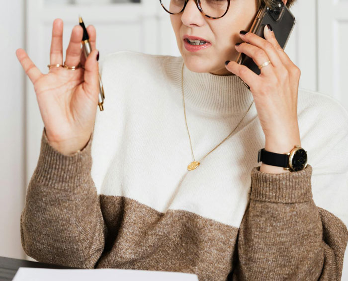 Woman in sweater on phone, gesturing with pen, discussing family event plans; refuses to babysit after argument.