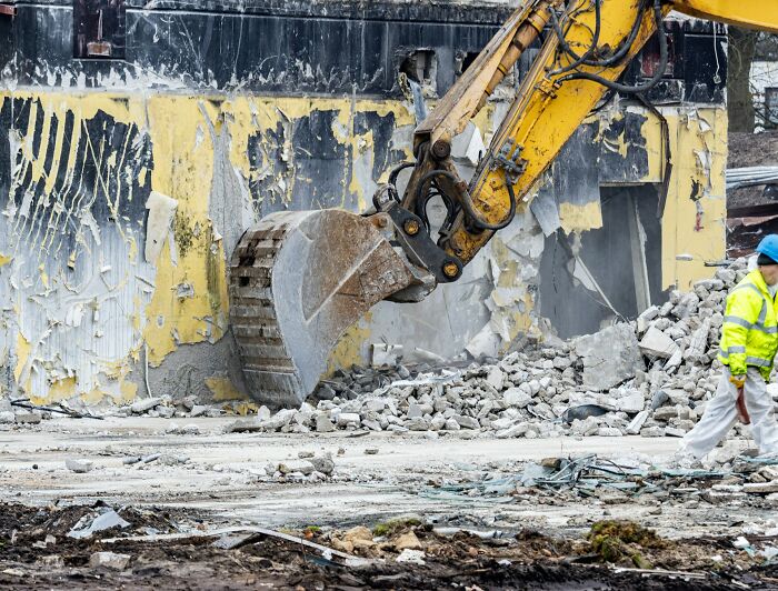 Construction worker beside a large excavator clearing debris, illustrating the reality of seemingly fun jobs.