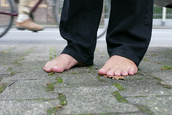 Barefoot person in jeans standing on a sidewalk, near a passing bicycle, symbolizing sudden job loss.