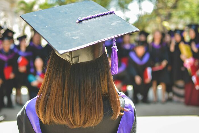 Graduate in cap and gown facing a group, illustrating rich kids unaware of real-world challenges.