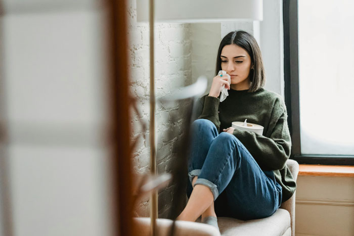 Woman named Dove sits thoughtfully, holding a cup, in a cozy living room setting.