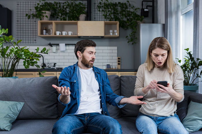 A couple having an intense discussion on the couch, surrounded by modern kitchen decor.