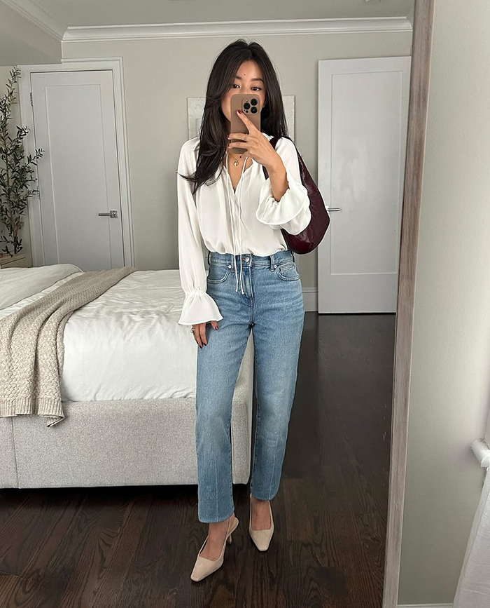 Woman in casual outfit taking a selfie in a bedroom setting.