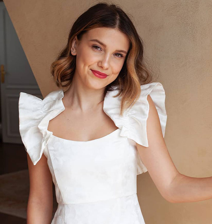 Young woman in a white dress with puffed sleeves, posing indoors.