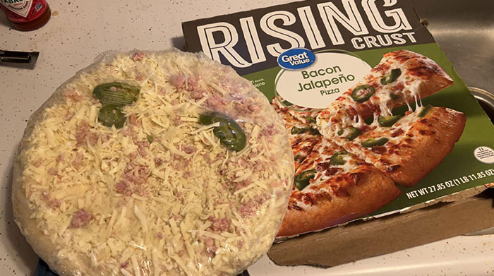 Pizza with sparse toppings next to a box showing a fully topped pizza, illustrating misleading packaging design.