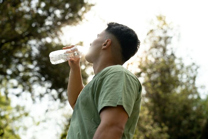 A man in a green shirt drinks water outdoors, highlighting the importance of exercise.