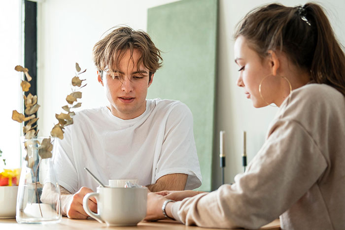 Young man discussing family dynamics with woman at a table, addressing assumptions about his sexuality.