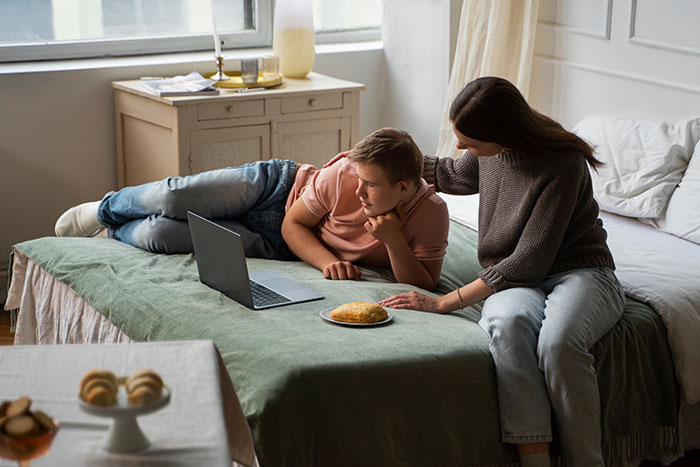 Young man on bed with laptop, being comforted by family, illustrating family drama dynamics.