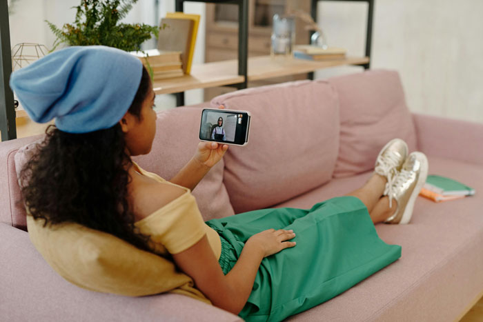 Woman relaxing on a couch, watching a video on her phone, possibly about mom-relationship-drama.