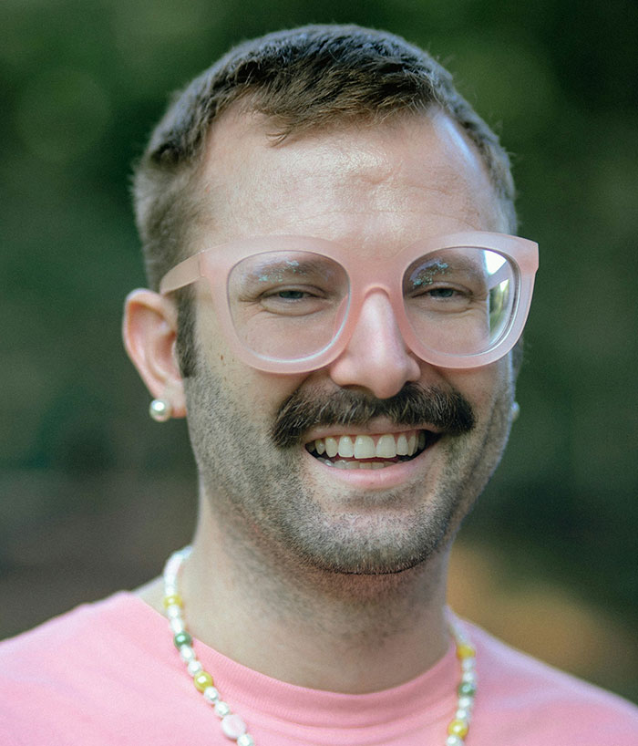 Person smiling, wearing large glasses and a pink shirt, representing gifted stereotype challenges.