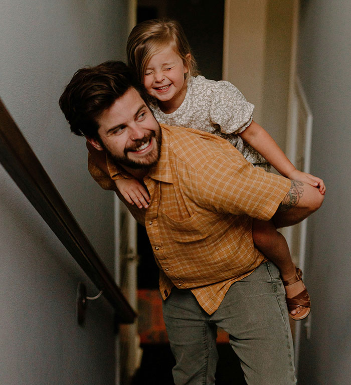 Man carrying smiling child in a hallway, highlighting stereotypes associated with being "born gifted."