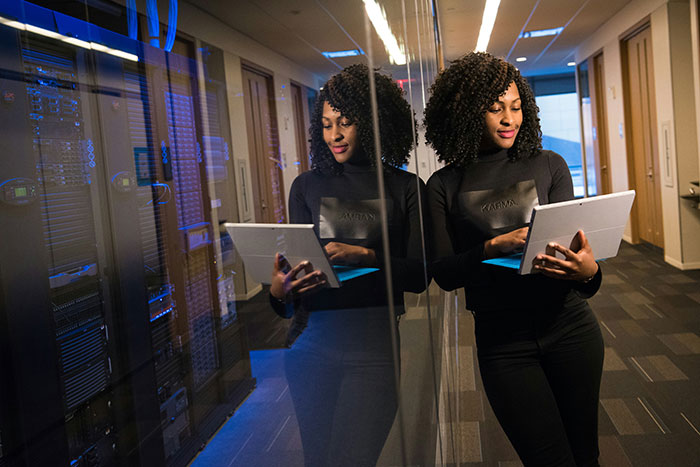 Woman with a tablet in a modern office hallway, reflecting on misconceptions about being "born gifted."