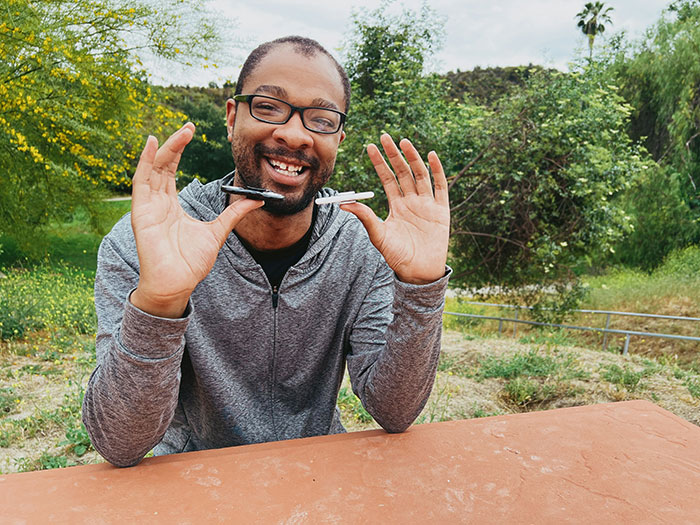 Man smiling outdoors, holding pens; challenges "born gifted" stereotypes in a casual setting.