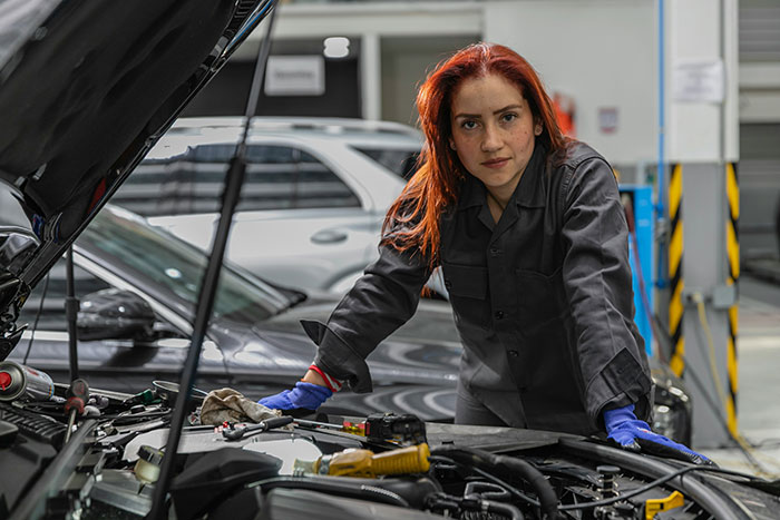 Woman challenging stereotypes, confidently working on a car engine in a garage, highlighting misconceptions.