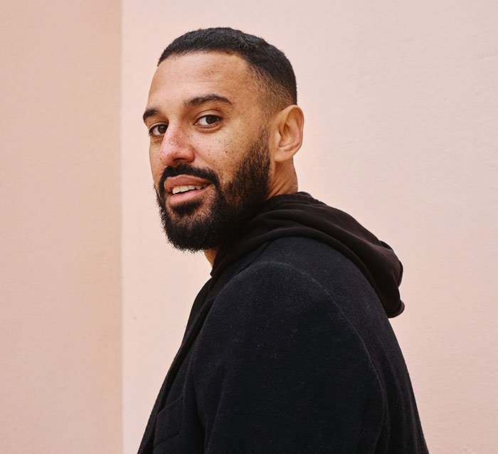 Man in a black hoodie against a pink wall, challenging stereotypes about being "born gifted."