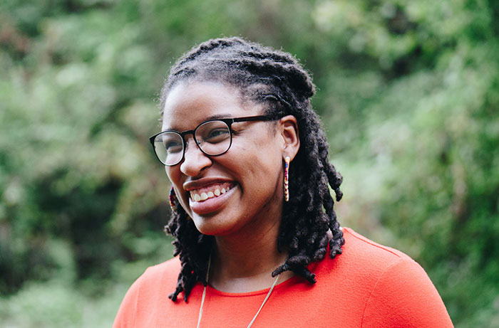 Person in glasses and red top, smiling outdoors, challenging "Born Gifted" stereotypes.