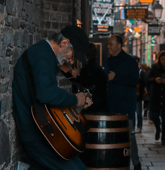 Street musician playing guitar, people passing by, illustrating "Born Gifted" stereotypes.