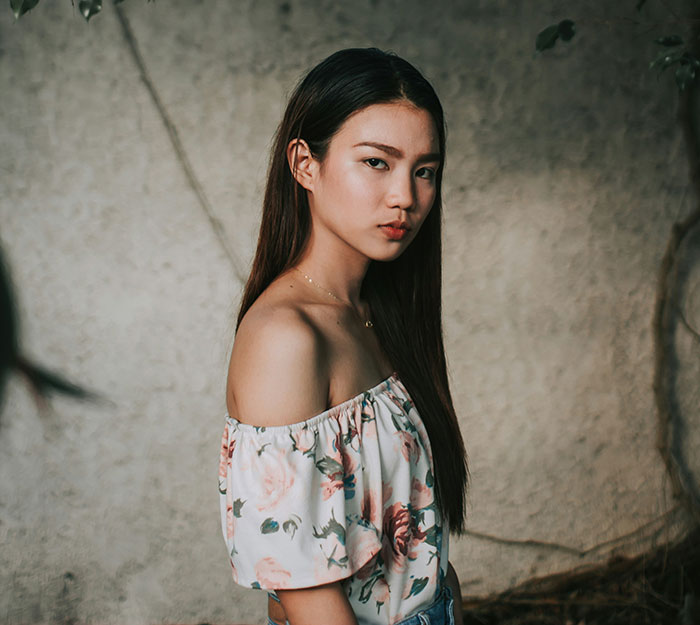 Young woman in a floral top standing against a textured wall, challenging gifted stereotypes.