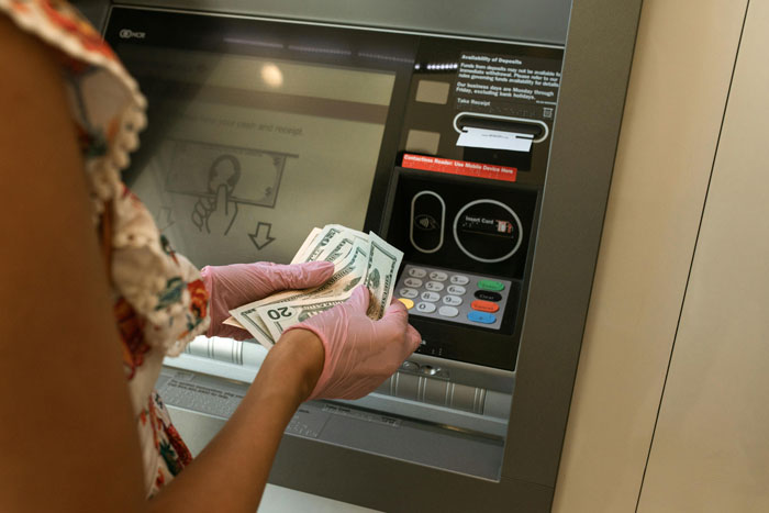 Woman withdrawing cash from ATM for a family emergency, holding dollar bills.