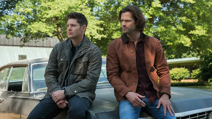 Two men sitting on a car hood, outdoors, highlighting movies' portrayal of gender roles and their impact on women.