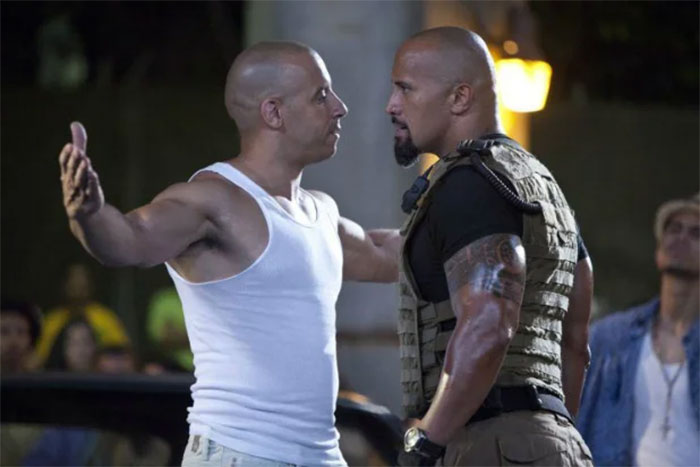 Two men facing off in a tense scene, wearing a white tank top and tactical gear, discussing poor portrayal of women in movies.